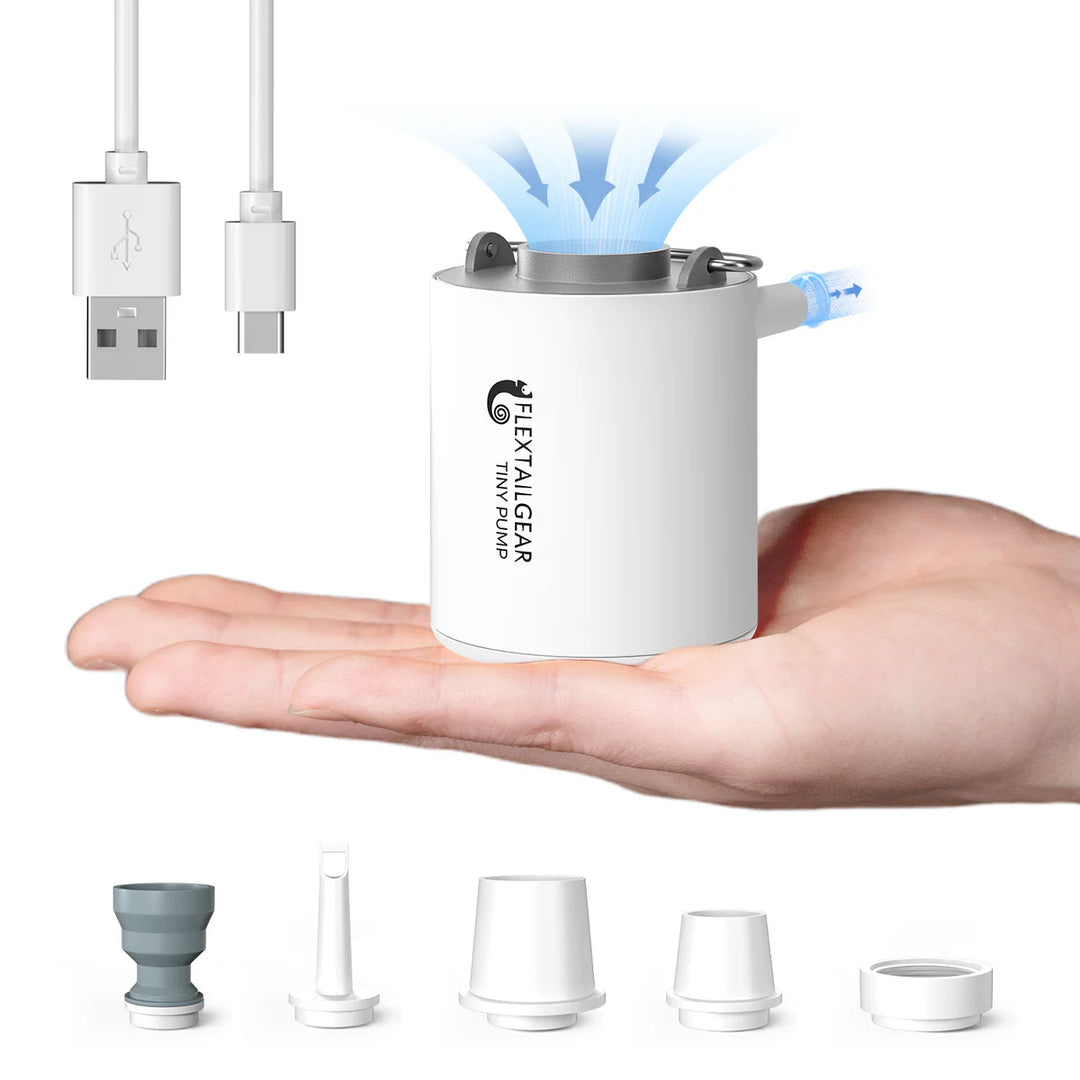 A compact white Flextail Tiny Pump Electric Air Pump by Flextail rests on an open hand with blue mist above. Below are a USB charging cable and four nozzle attachments—perfect for outdoor adventure lovers.