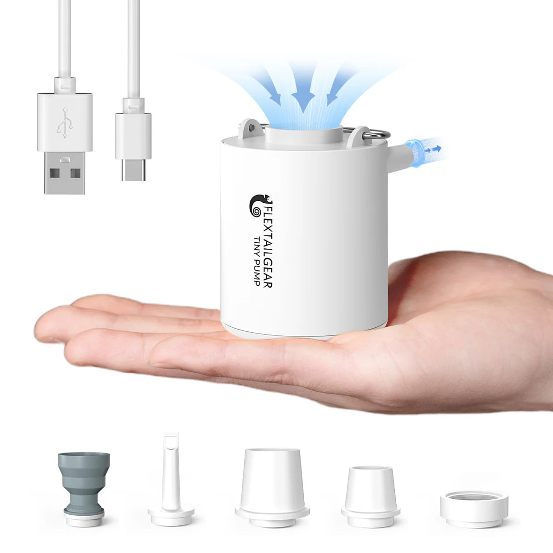 A compact white Flextail Tiny Pump Electric Air Pump by Flextail sits on a hand, releasing blue air or water streams from the top. Rapid inflation is simple, with various nozzles and USB cables shown—perfect for outdoor enthusiasts.